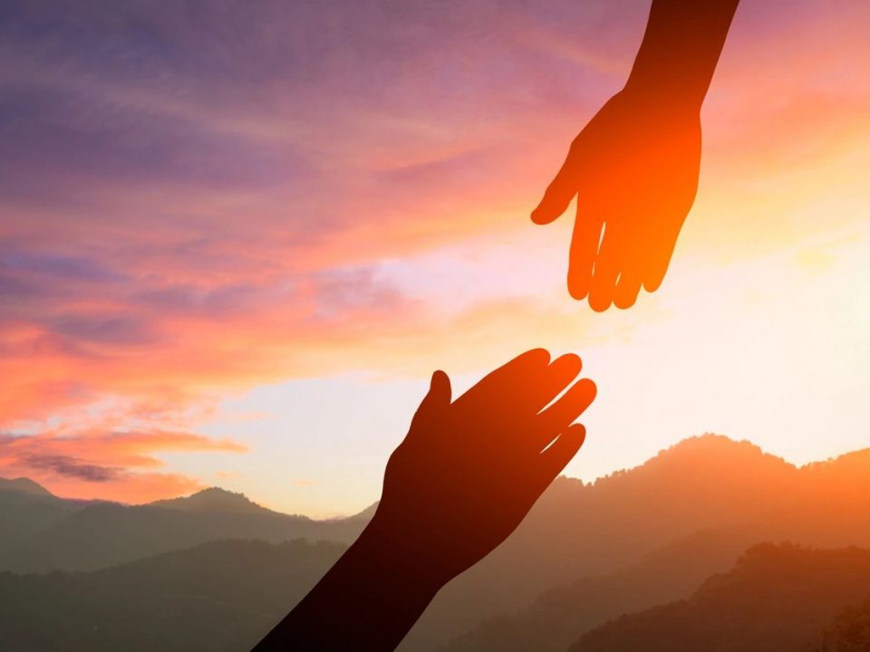 a photo of two hands reaching for each other in the sunset